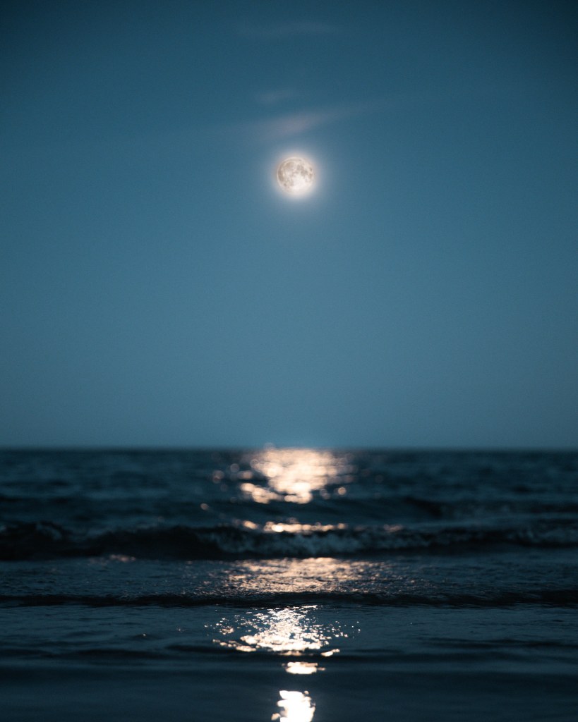 Calm sea with waves reaching the shore towards you with the wavy reflection of the full white moon